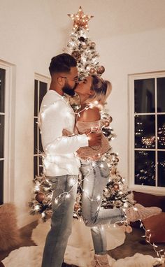 a man and woman kissing in front of a christmas tree with lights all around them