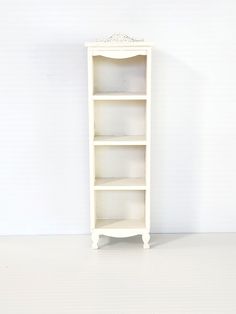 a white bookcase with three shelves on the bottom and one shelf below it, against a wall