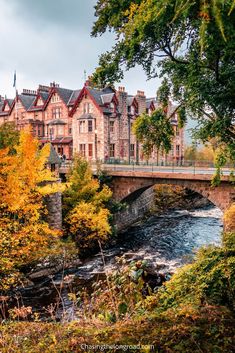 a bridge over a river in front of a building with autumn foliage on the ground