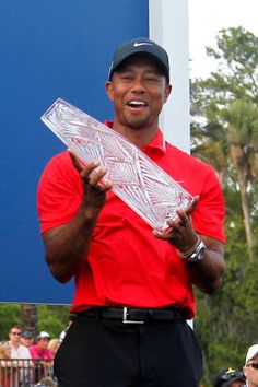 the man is holding his trophy in one hand and wearing a red shirt with black pants