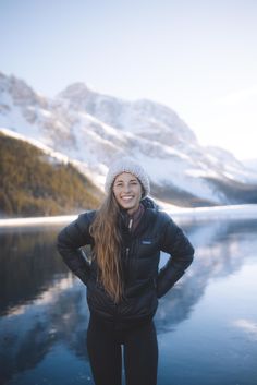 a woman standing on the edge of a lake with her hands on her hips and smiling