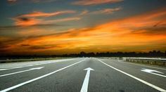 an empty road with white arrows painted on it at sunset or sunrise in the sky