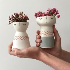 two white vases with pink flowers in them are being held by someone's hand