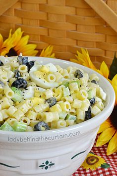 a white bowl filled with pasta salad next to yellow sunflowers and a basket