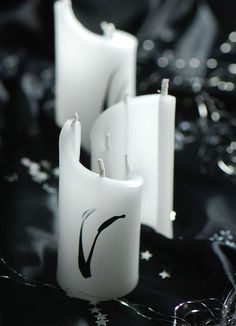 two white candles sitting next to each other on a black cloth covered table with water droplets