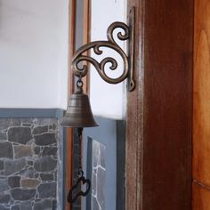 a bell hanging from the side of a door next to a stone wall and wooden door