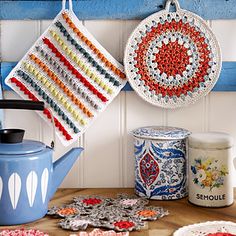 two crocheted potholders hanging on a wall next to a blue teapot