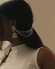 a woman with long black hair wearing gold and silver earrings on her head, standing in front of a white wall