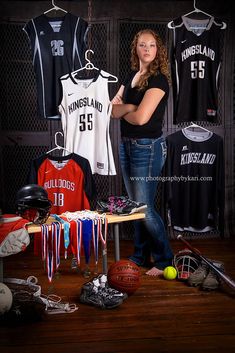 a woman standing next to a table with basketballs and jerseys on it in front of a wall