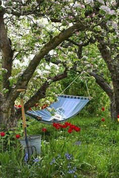 an empty hammock in the middle of a garden with flowers and trees around it