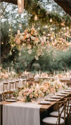 an outdoor dinner table with candles and flowers hanging from the ceiling, surrounded by greenery