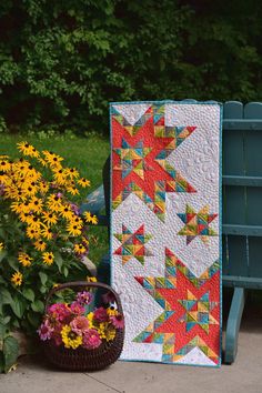 a colorful quilt sitting on top of a wooden bench next to flowers and a basket