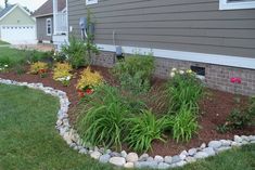 a flower bed in front of a house with rocks and flowers growing on the ground