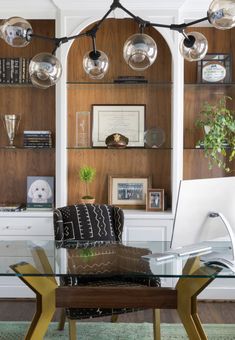 a glass table in front of a wooden wall with hanging lights above it and bookshelves