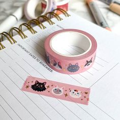 a pink washi tape with cats and stars on it next to a spiral notebook