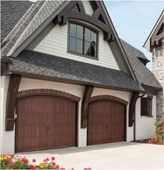 two brown garage doors are open in front of a white house with red flowers on the side