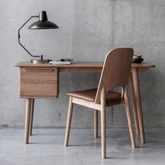 a wooden desk with a chair and lamp on it in front of a concrete wall