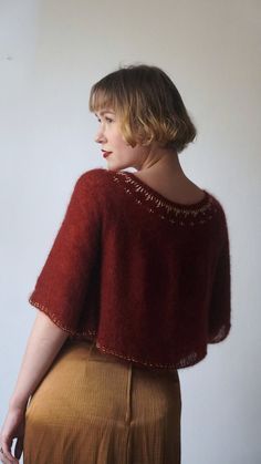 a woman standing in front of a white wall wearing a red sweater and brown skirt