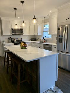 a kitchen with white cabinets and an island in front of the stove, refrigerator and dishwasher