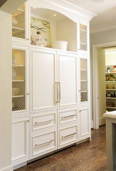 a large white cabinet with glass doors in a kitchen next to a sink and counter