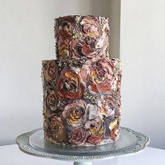 a three tiered cake decorated with flowers on a blue plate next to a white wall