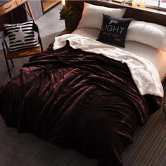 a bed with a red comforter and two pillows on it, next to a chair