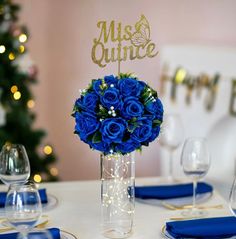 a centerpiece with blue roses in a clear vase on a table set for an event