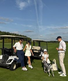 three people and two dogs are standing in the grass near a golf cart on a course