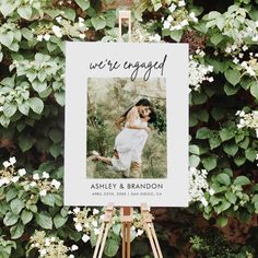 an easel with a wedding photo on it in front of some flowers and greenery