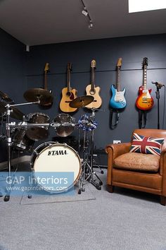 a room filled with guitars and drums on the wall next to a leather chair in front of it