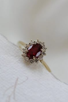 a close up of a ring with a red stone in the center on a white cloth