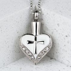 The elegant Cross My Heart stainless steel cremation pendant is a beautiful way to remember your dear departed loved one. The silver of the steel is highlighted by an elegant white enamel center that surrounds a silver colored cross. It also features a number of cubic zirconia stones along the bottom of the heart. This keepsake pendant can hold a small portion of cremated remains, a lock of hair, or dried ceremonial flowers. White Heart Pendant Jewelry For Memorial, White Heart Necklace For Keepsake, White Heart Pendant Necklace For Keepsake, White Necklace For Memorial On Valentine's Day, Cremated Remains, Personalized Memorial Gifts, Lock Of Hair, Cremation Necklaces, Pet Sympathy Gifts