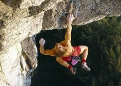 a man climbing up the side of a cliff with his hands in the air while wearing red shorts