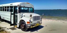 a white school bus parked on the side of the beach near the water and sand