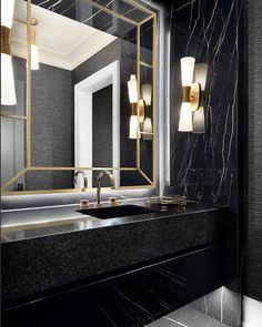 a bathroom with a marble counter top and gold accents on the mirror, along with two wall sconces