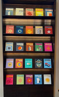 a book shelf filled with lots of different colored books on top of wooden shelves next to a white wall