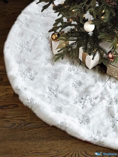 a christmas tree with presents under it on a white round tablecloth covered in snow