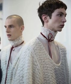 two men in white sweaters with red ties and collars standing next to each other