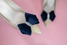 a pair of blue and white shoes with bows on the heel, against a pink background