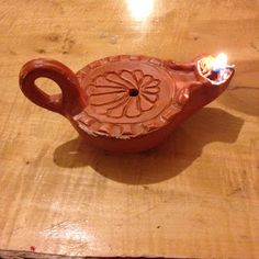 a small clay teapot with a lit candle in the middle on a wooden table