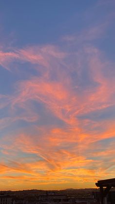 the sky is very colorful at sunset with some clouds in the foreground and buildings on the other side