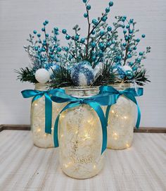 three mason jars decorated with blue and white christmas decorations, one is filled with lights