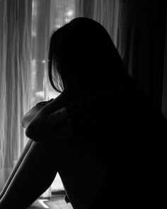 a woman sitting in front of a window with her hands on her knees and looking out the window