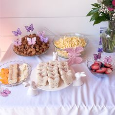 a table topped with lots of desserts and flowers on top of a white table cloth