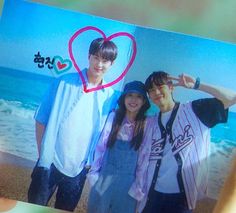 two people are holding up a photo with a heart on the beach in front of them