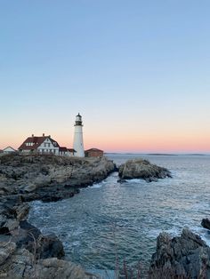 a light house sitting on top of a rocky cliff next to the ocean at sunset