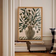 a vase filled with green leaves sitting on top of a wooden floor next to a pile of books