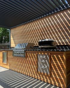 an outdoor bbq with grill and counter space under a pergolated awning