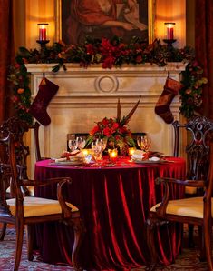 a dining room table set for christmas with candles and stockings on the mantel above it