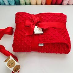 a red blanket with a bow on it next to some colored crochet yarn